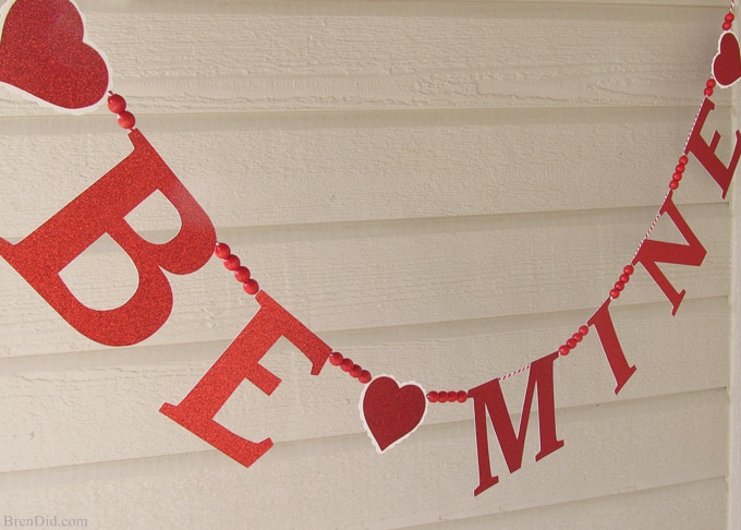 Get ready for Valentine's Day parties and events with this glitter garland inspired by Pottery Barn Kids. This easy Knock Off DIY craft uses glitter cardstock, some twine, and wooden beads to make a charming Valentine's Day banner for under $3.