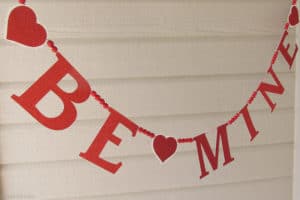 Get ready for Valentine's Day parties and events with this glitter garland inspired by Pottery Barn Kids. This easy Knock Off DIY craft uses glitter cardstock, some twine, and wooden beads to make a charming Valentine's Day banner for under $3.