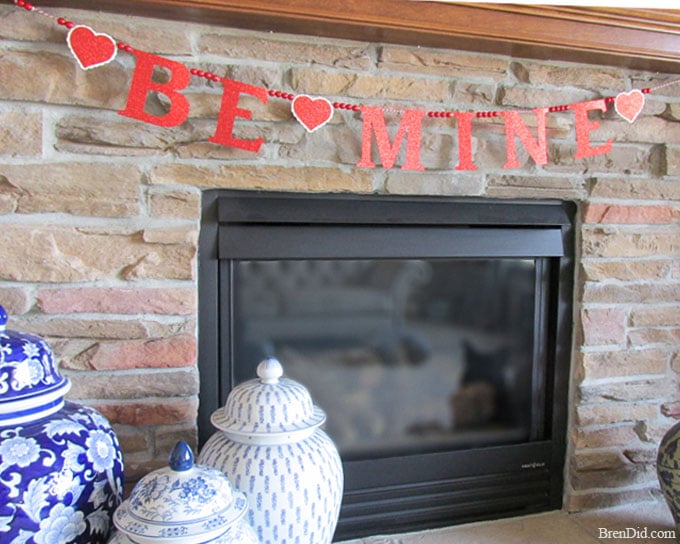 Get ready for Valentine's Day parties and events with this glitter garland inspired by Pottery Barn Kids. This easy Knock Off DIY craft uses glitter cardstock, some twine, and wooden beads to make a charming Valentine's Day banner for under $3.