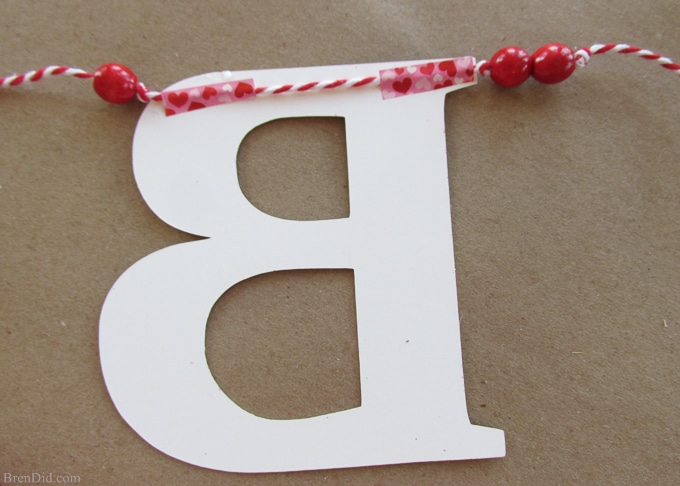 Get ready for Valentine's Day parties and events with this glitter garland inspired by Pottery Barn Kids. This easy Knock Off DIY craft uses glitter cardstock, some twine, and wooden beads to make a charming Valentine's Day banner for under $3.