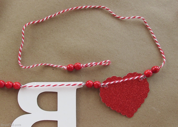 Get ready for Valentine's Day parties and events with this glitter garland inspired by Pottery Barn Kids. This easy Knock Off DIY craft uses glitter cardstock, some twine, and wooden beads to make a charming Valentine's Day banner for under $3.