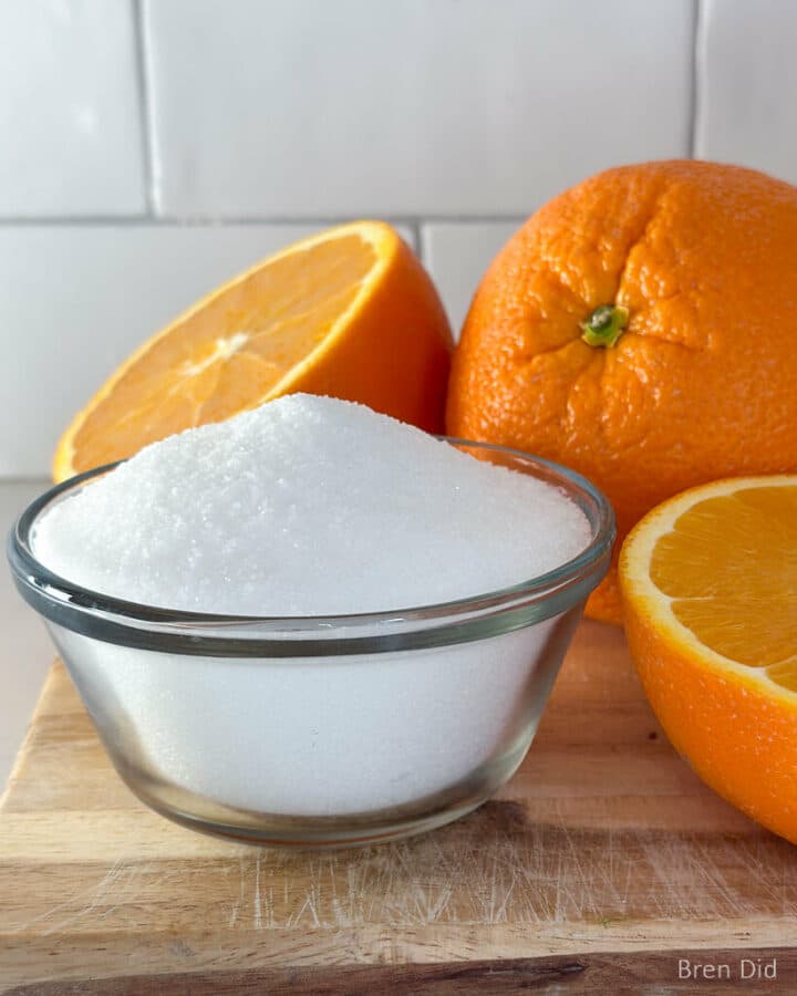 Powdered citric acid in a small glass bowl surrounded by oranges.