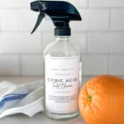 Citric acid toilet cleaner in a glass spray bottle with cleaning cloths.