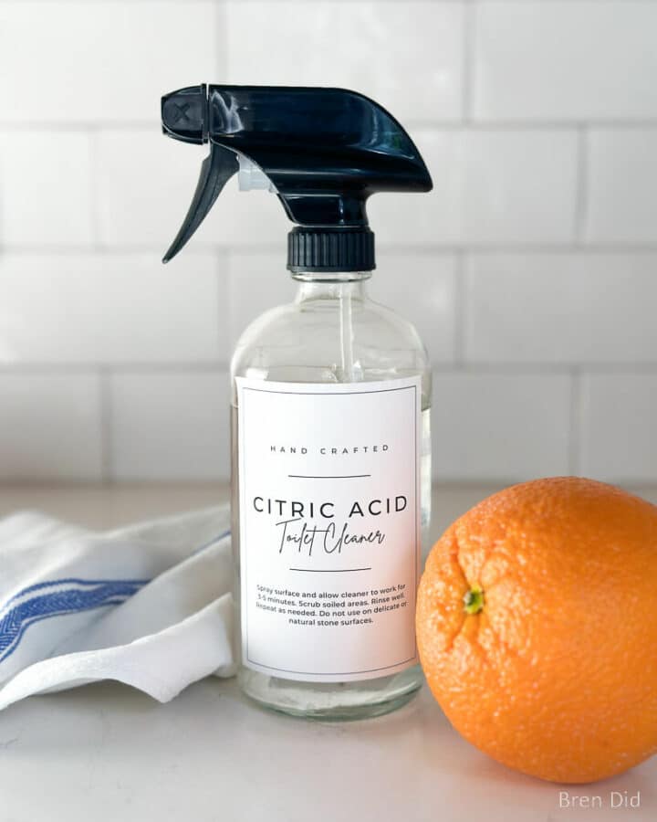Citric acid toilet cleaner in a glass spray bottle with cleaning cloths.