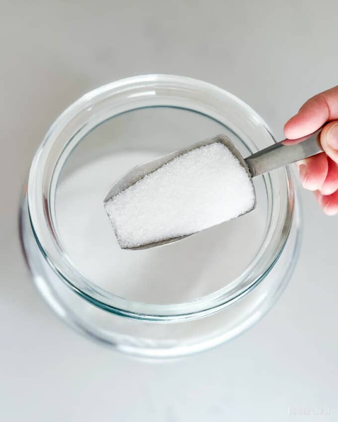 Powdered citric acid being scooped out of a glass jar.